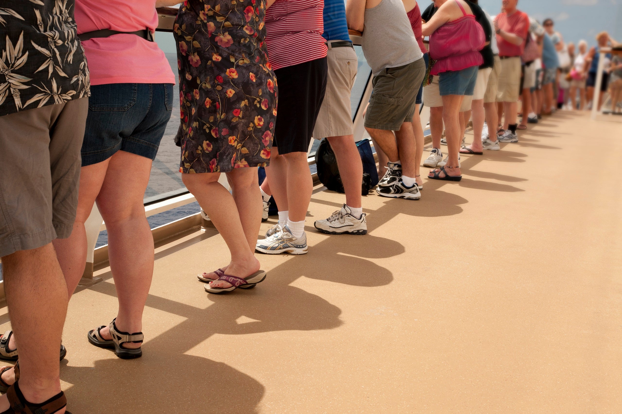 Cruise ship passengers standing along a deck railing wearing casual clothing