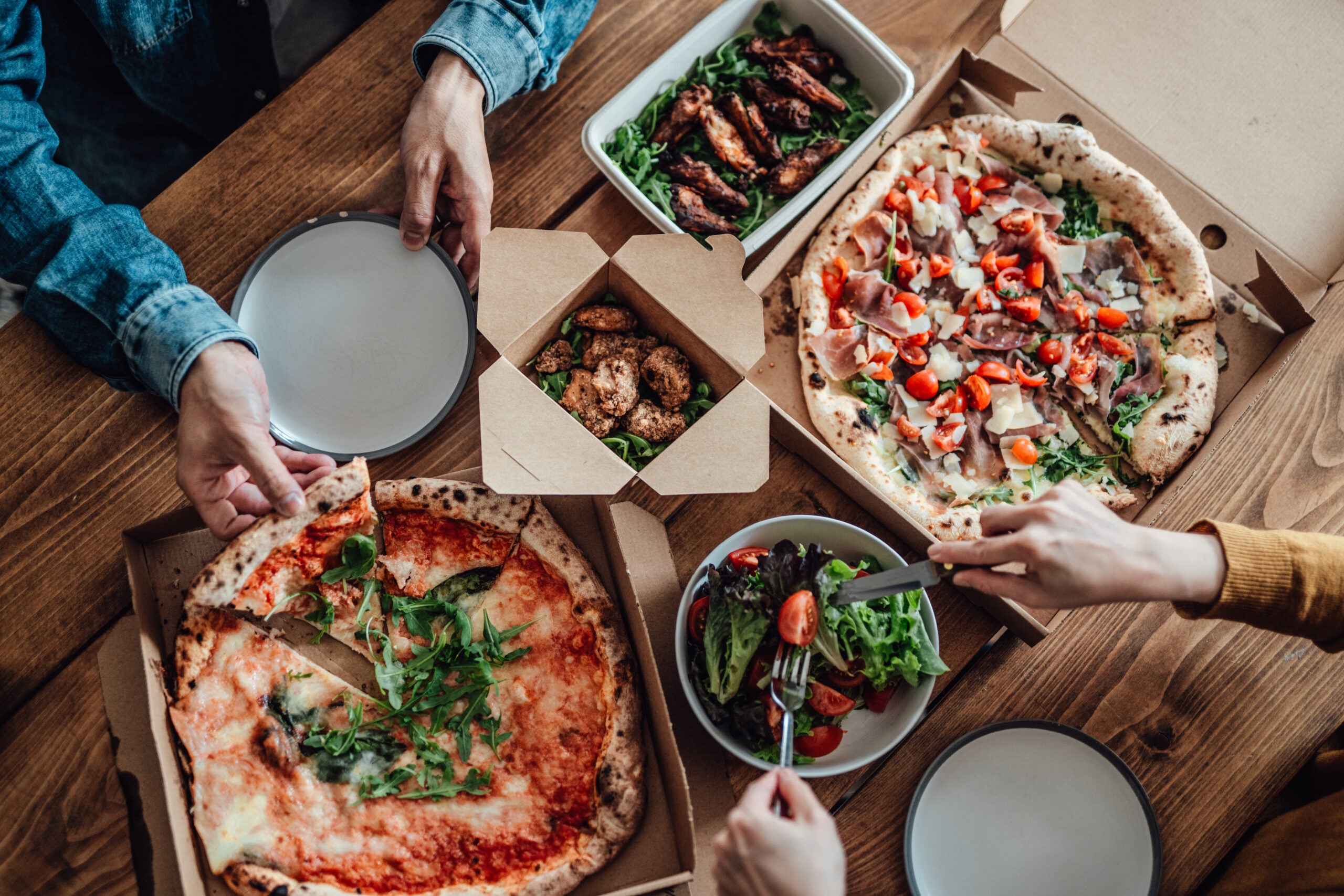 Overhead shot of woman eating green salad while sharing pizza at the dining table. Food delivery.