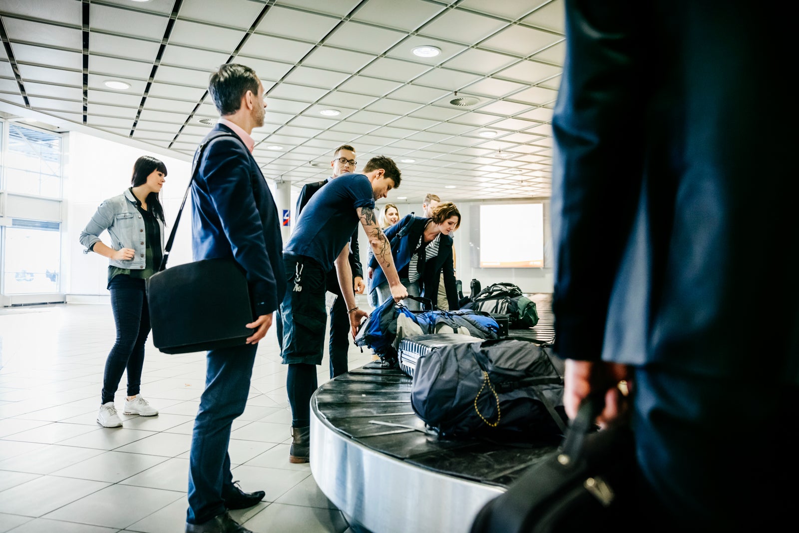 Travelers standing around a baggage claim carousel and reaching for bags