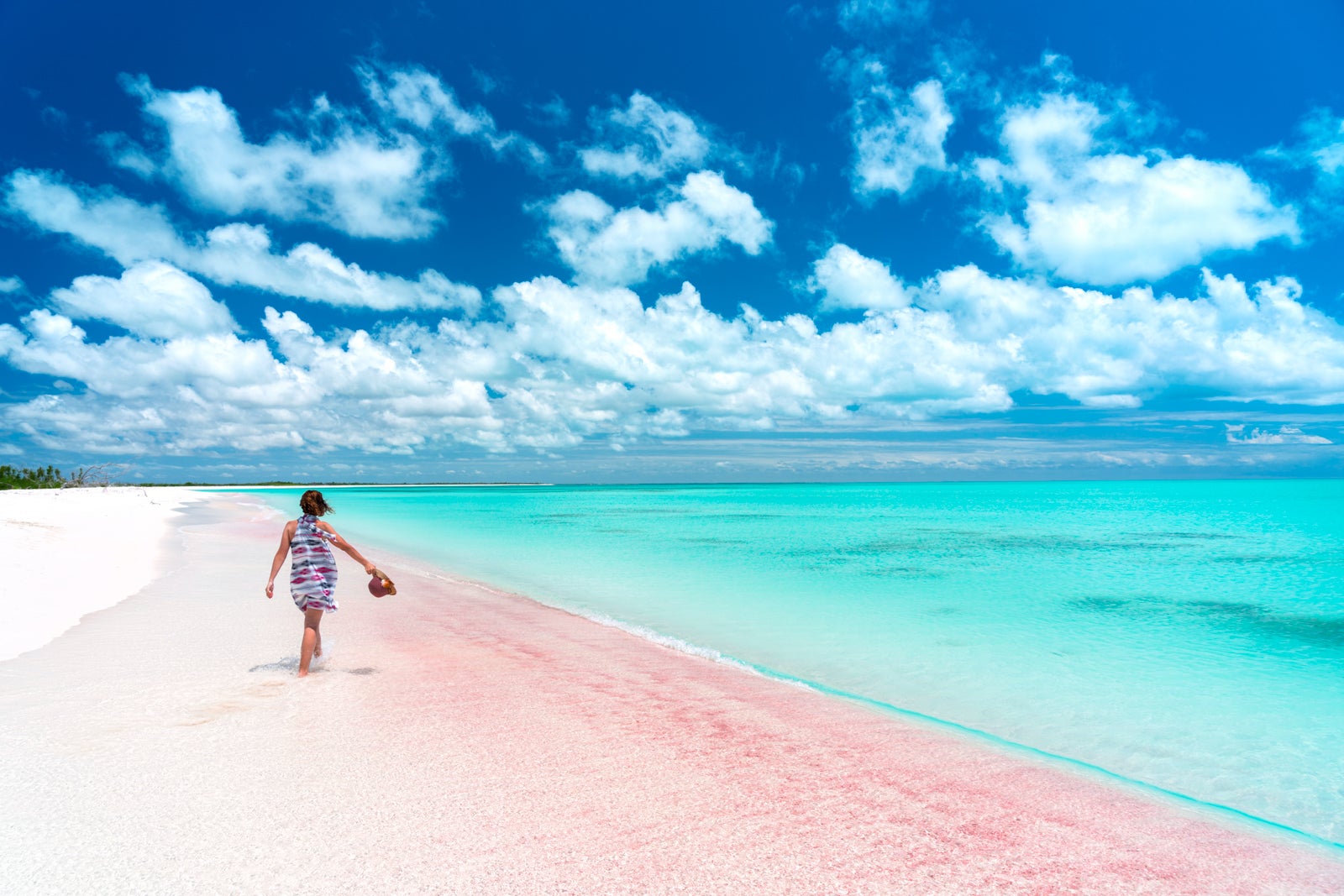 Woman walking along the water on pink sand beach in the Bahamas