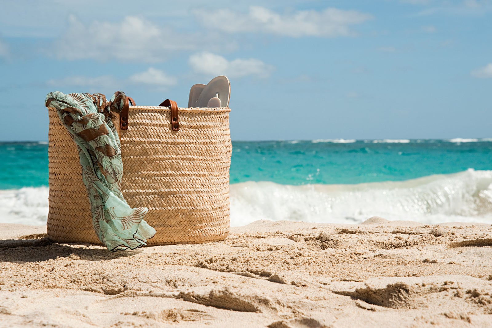 A straw beach bag sitting on the sand in front of the ocean