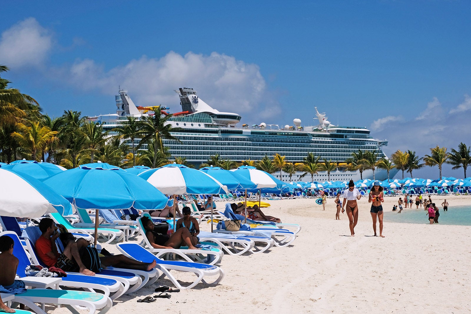 Crowded beach with chairs and umbrellas with cruise ship in the background