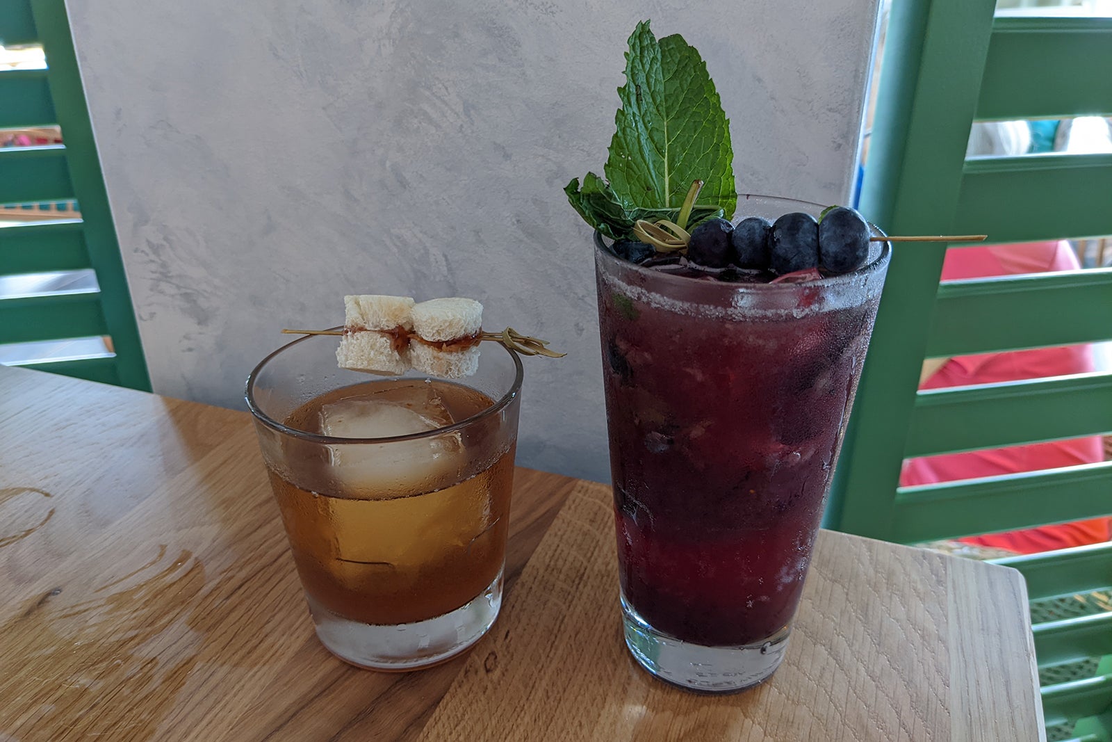 A whiskey cocktail and a tall blueberry cocktail on a table
