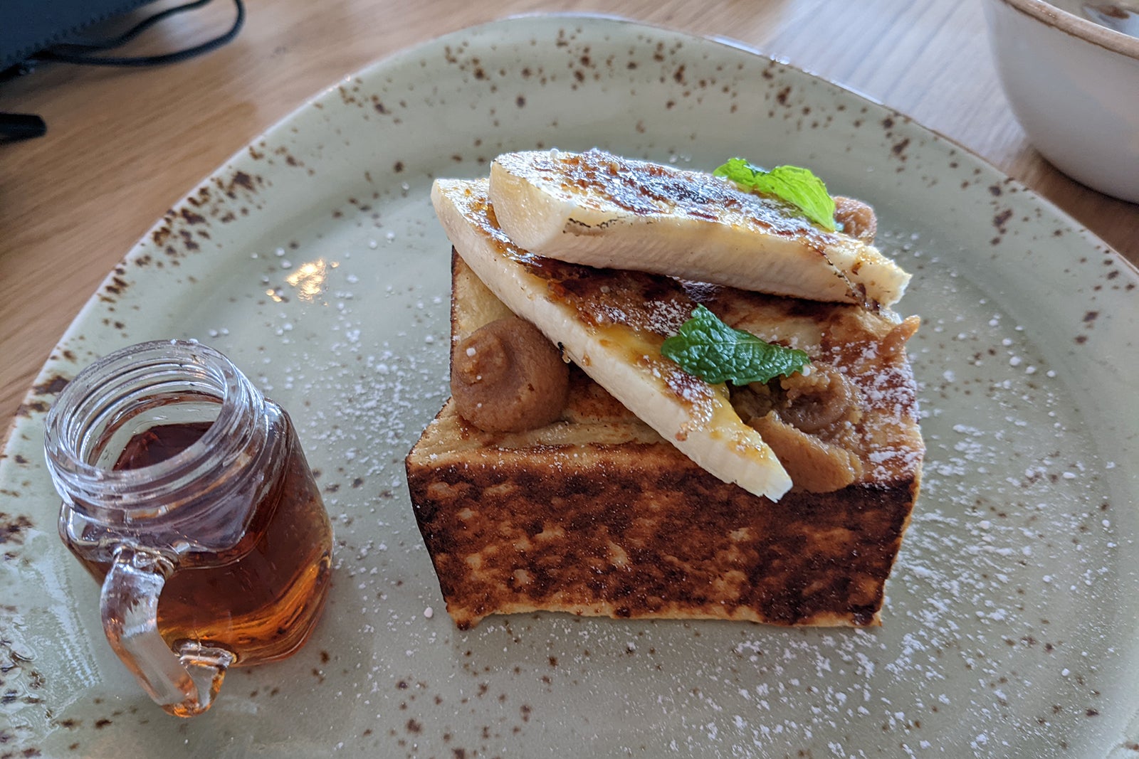 Stuffed French toast with a banana on top and small glass jar of syrup