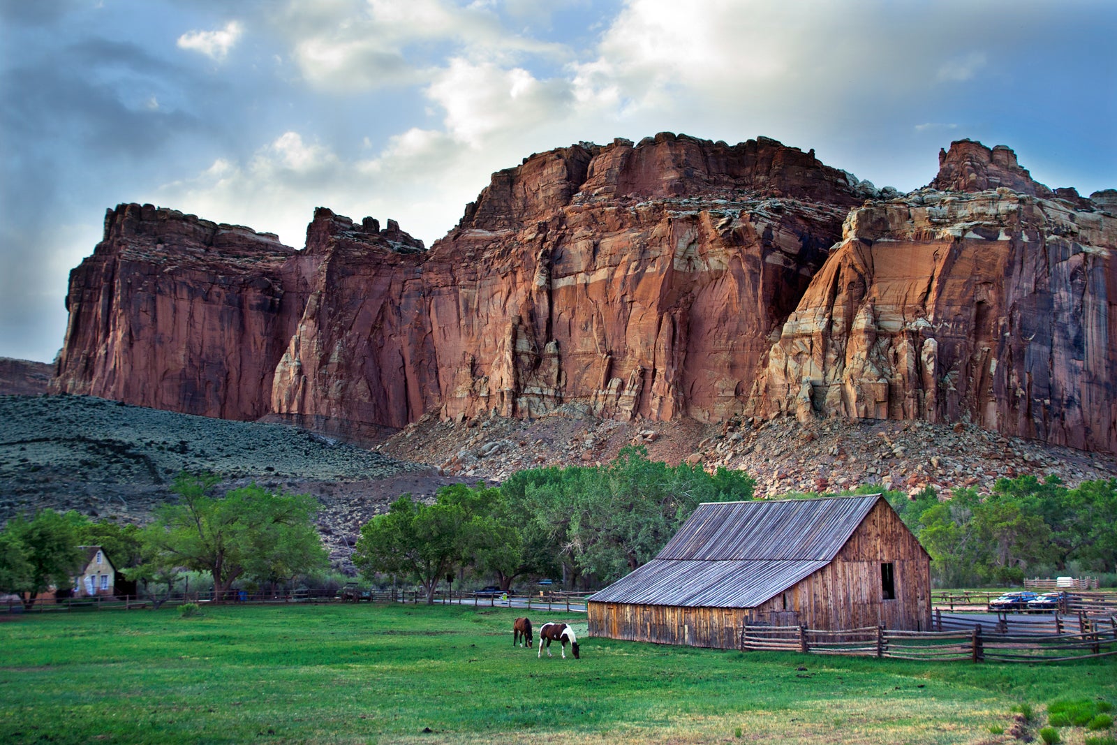 photo of cliffs and rock formations in the background with a cabin sitting in a green field in the foreground