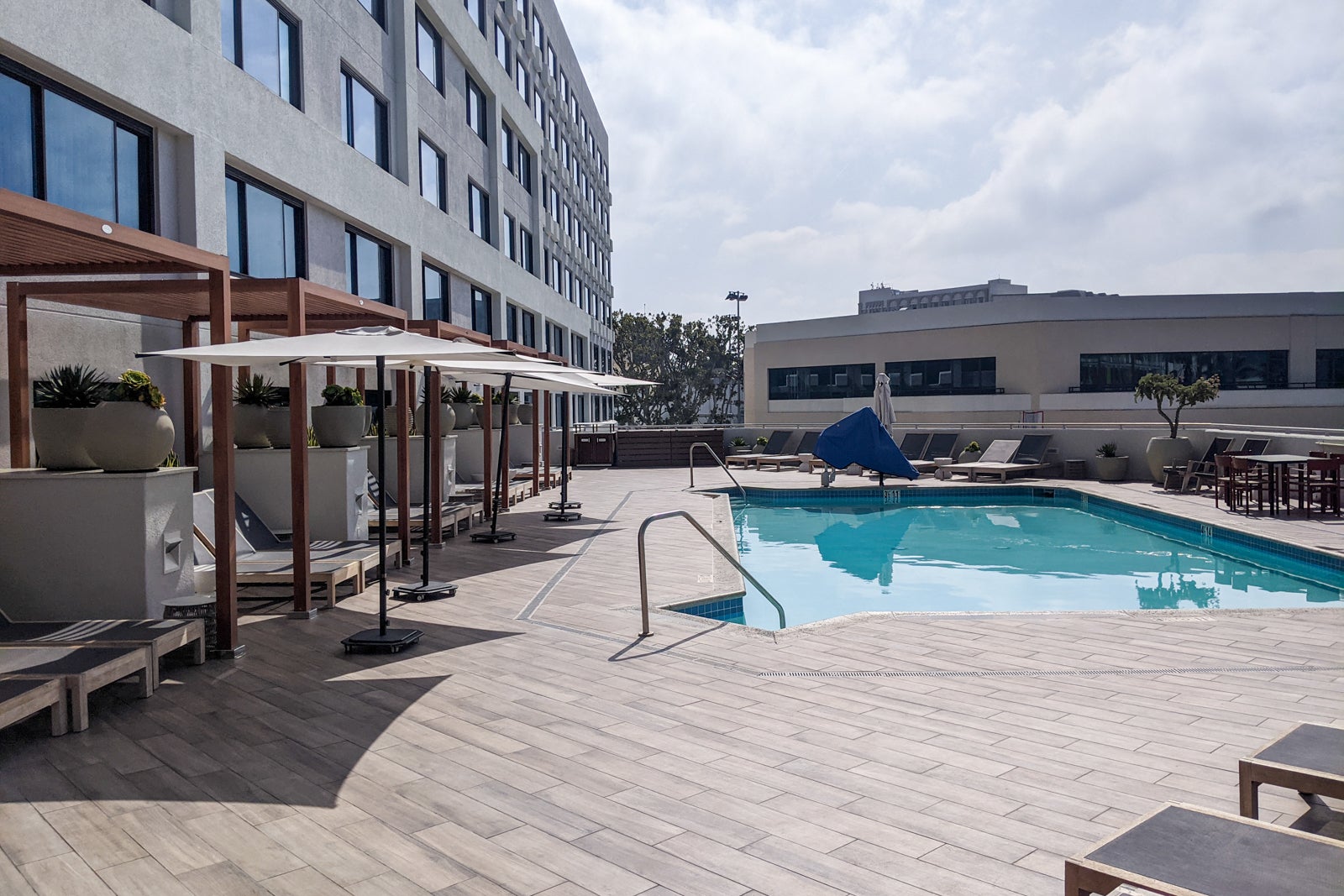 a hotel pool flanked by the hotel building and shade-covered lounge chairs