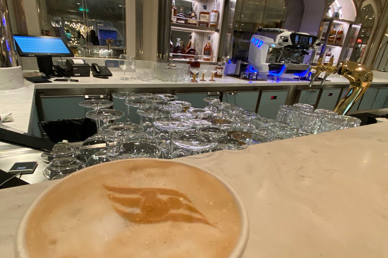 A photo of a coffee bar with the top of a specialty coffee in the lower left-hand corner covered with cinnamon in the shape ofo the Disney Cruise Line logo