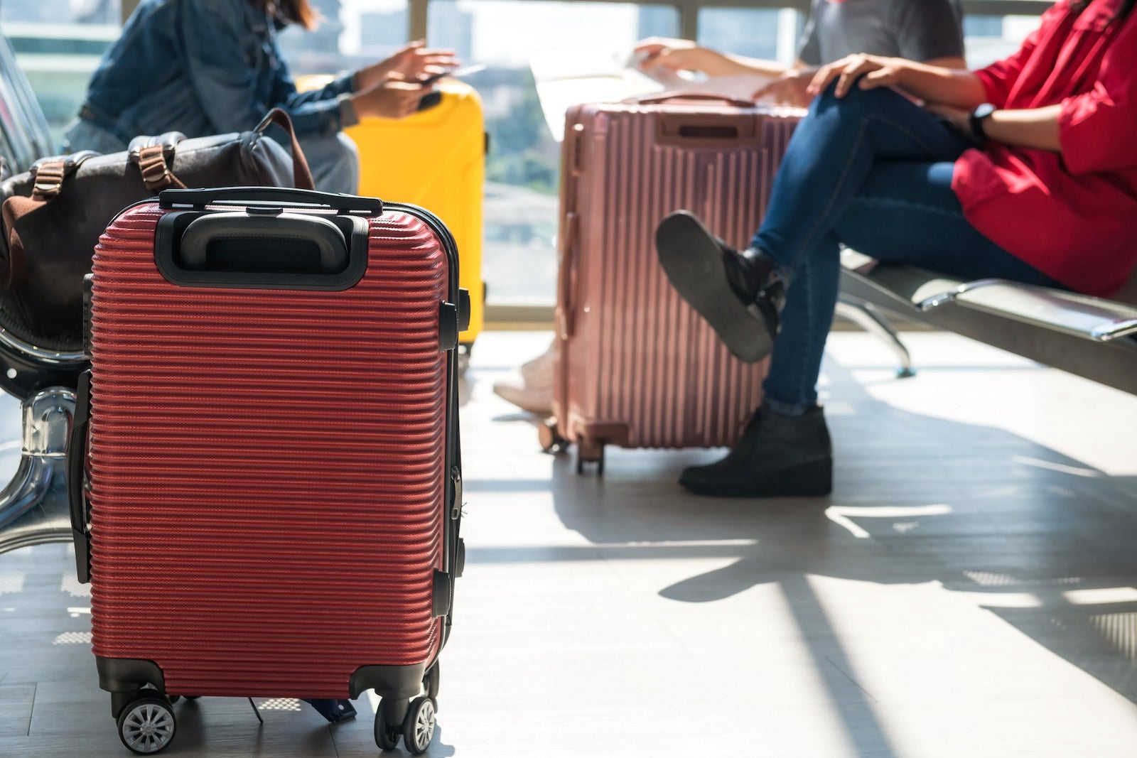 people with suitcases sit in chairs at an airport gate