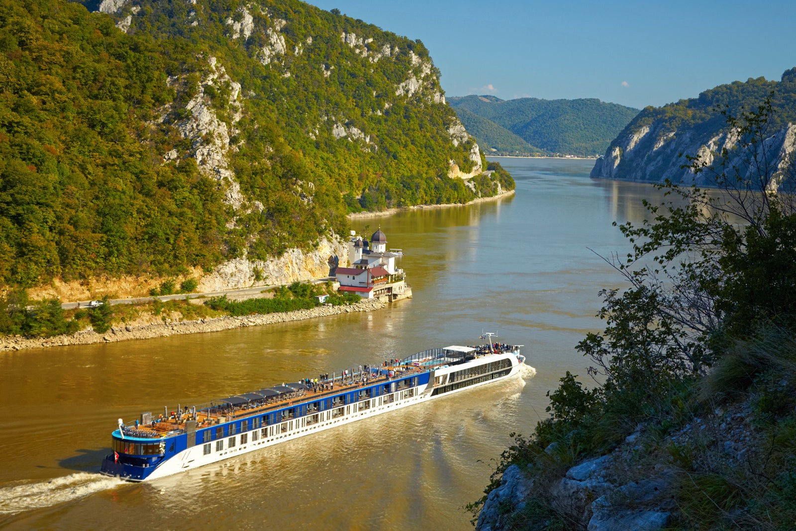 A river cruise ship sailing on the Danube River with mountains rising up on either side