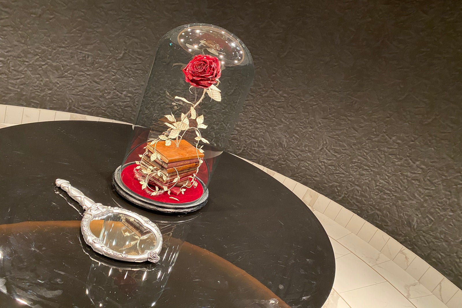 A table with a hand mirror and a glass case with a rose inside