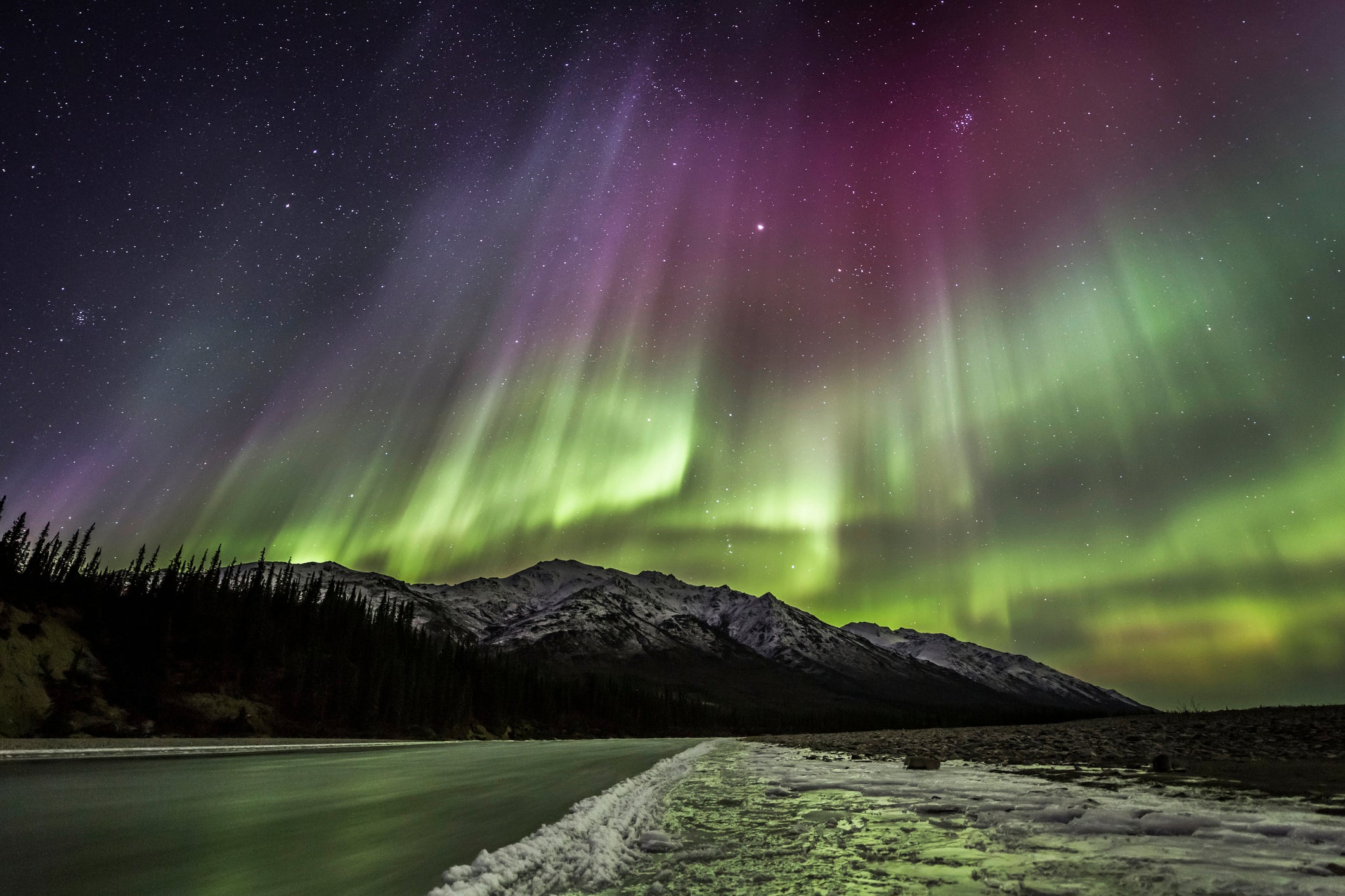 Northern lights shine brightly above a mountain and lake