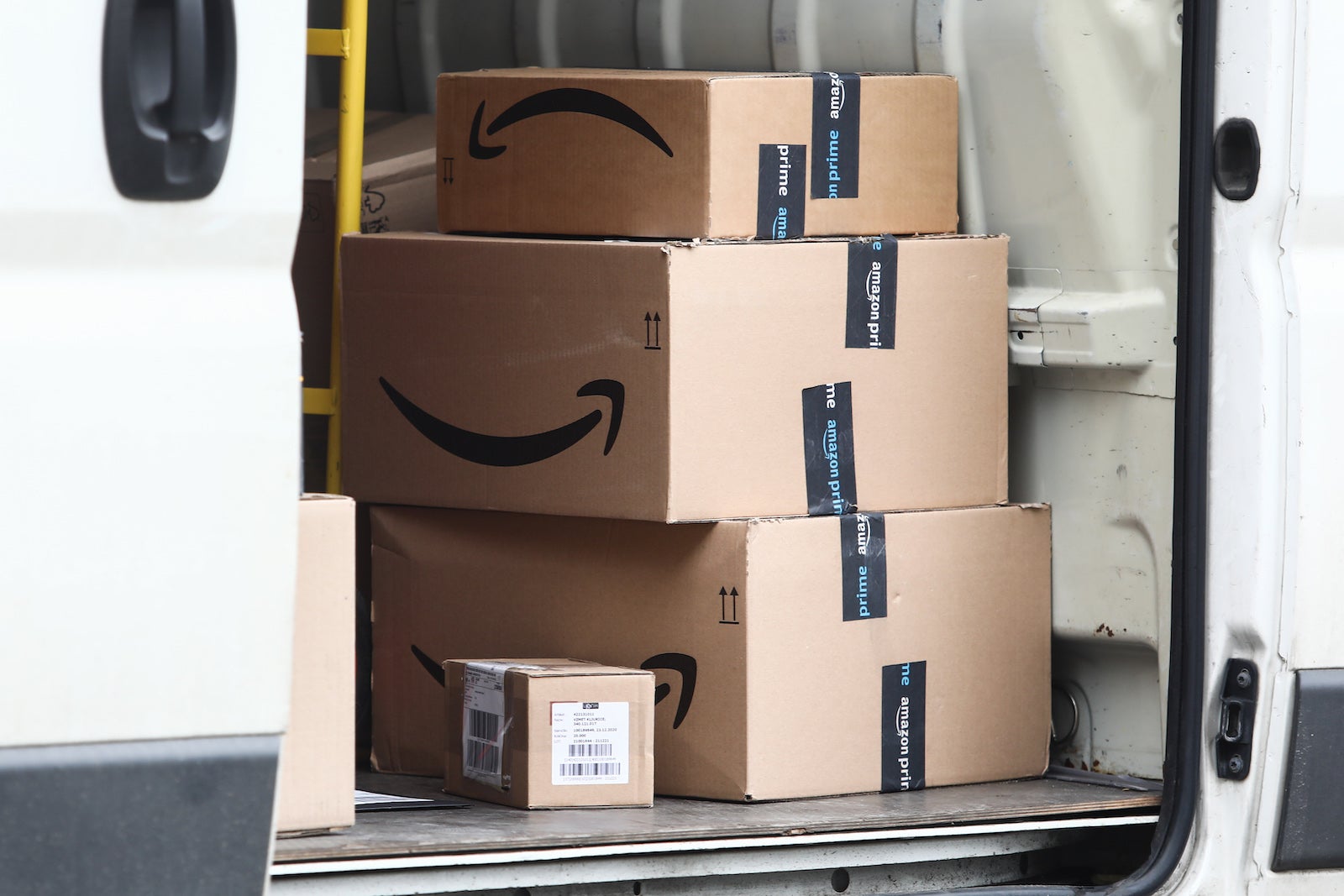 A stack of Amazon boxes sits in the back of a white van 