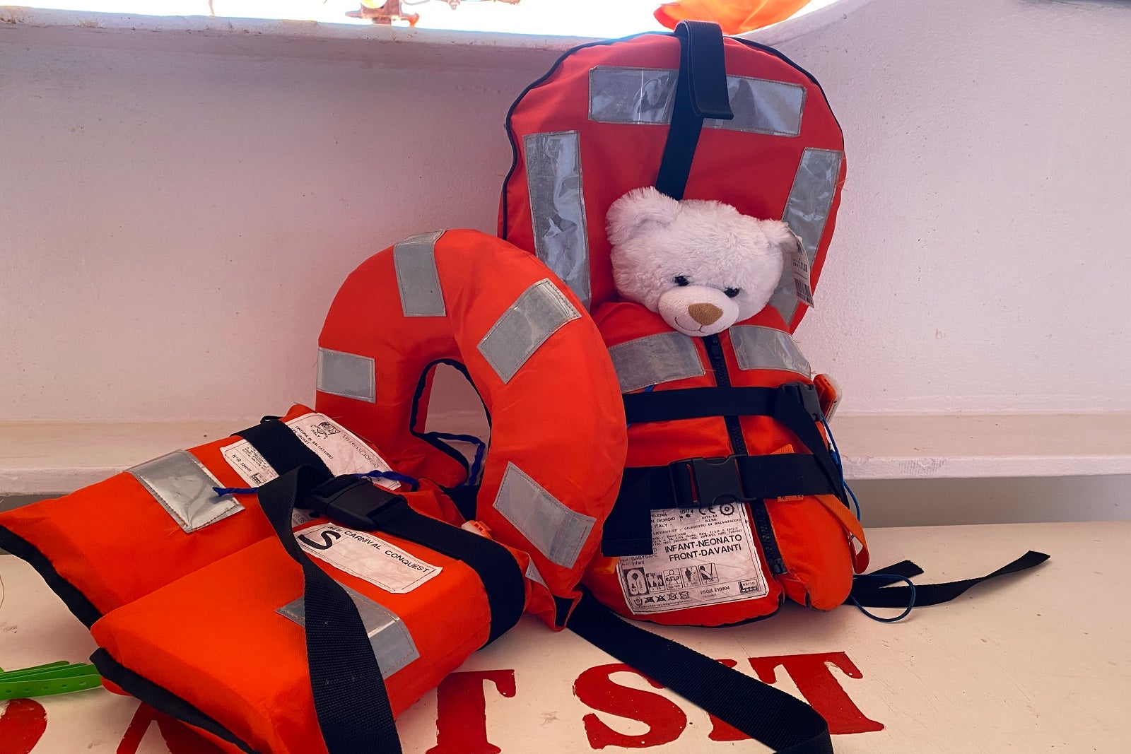 Two life jackets sitting on a counter on a cruise ship deck, one with a white teddy bear in it