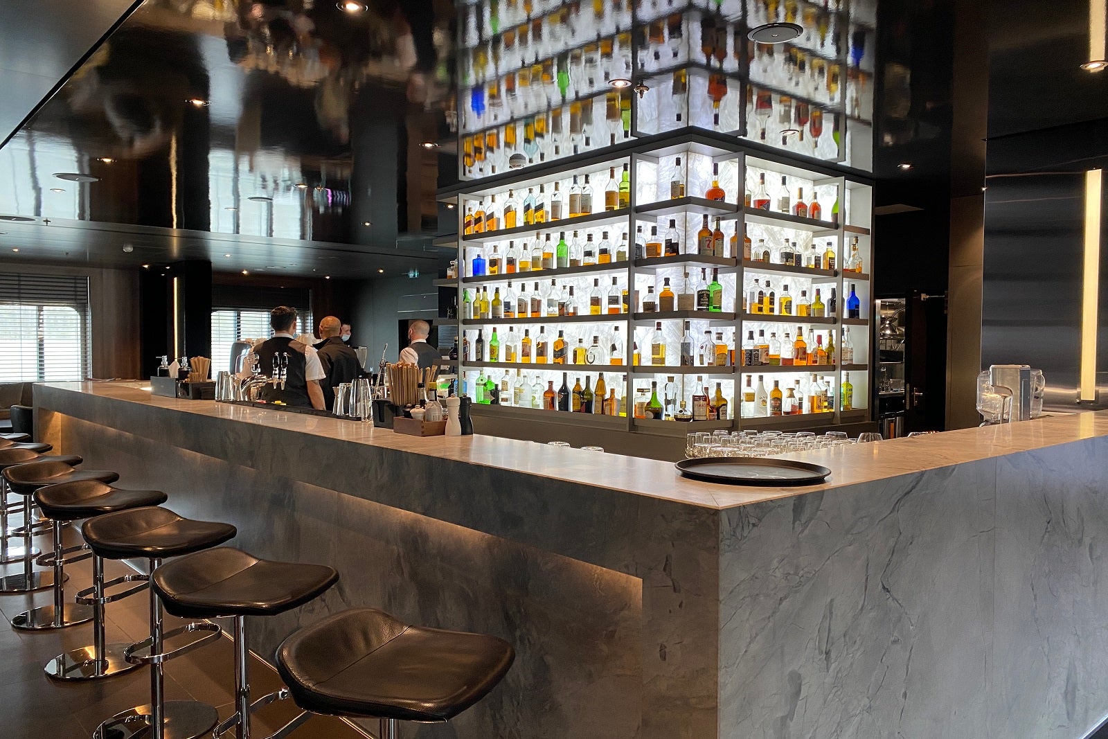 A large granite bar with chairs faces a floor-to-ceilling wall of shelves filled with whiskies from all over the world.