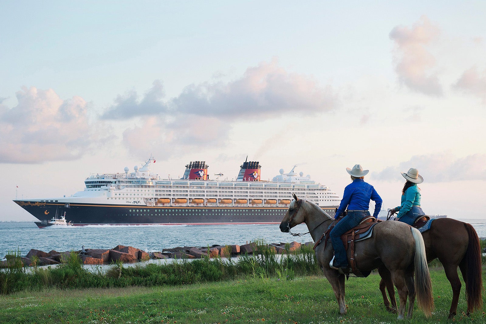 A man and woman wearing cowboy hats and sitting on horses watch Disney Magic cruise ship sailing into Galveston.