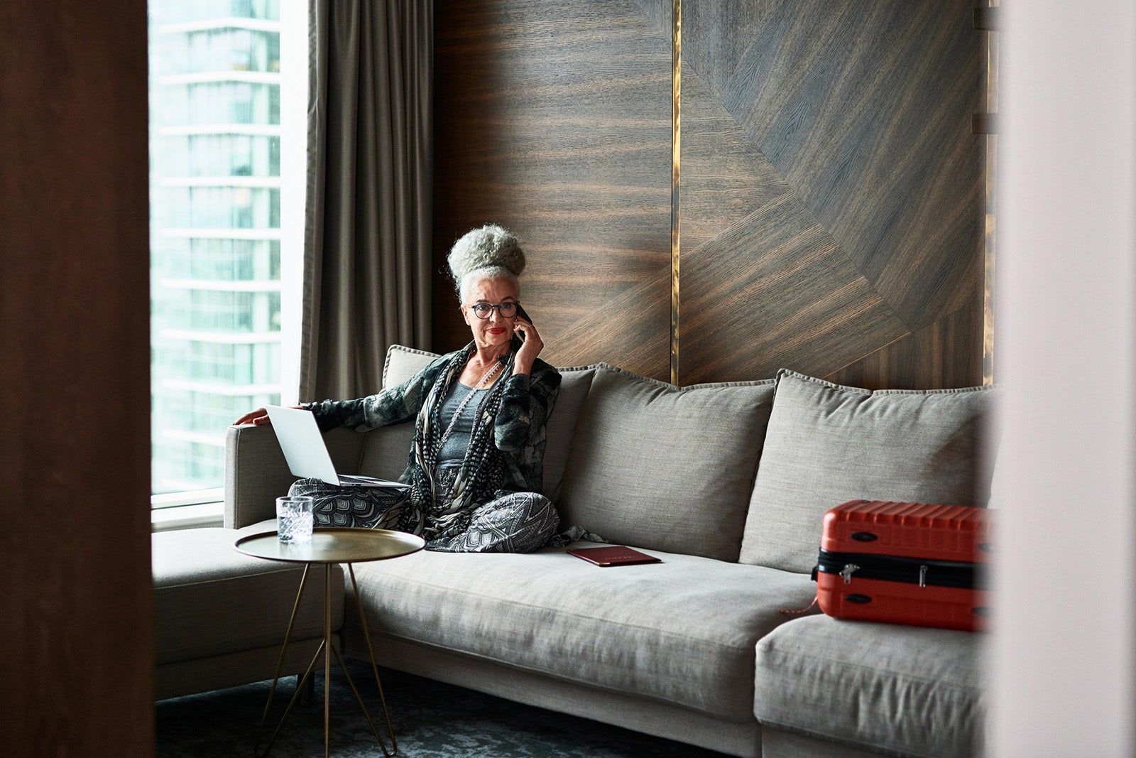 Senior woman using phone and laptop in boutique hotel
