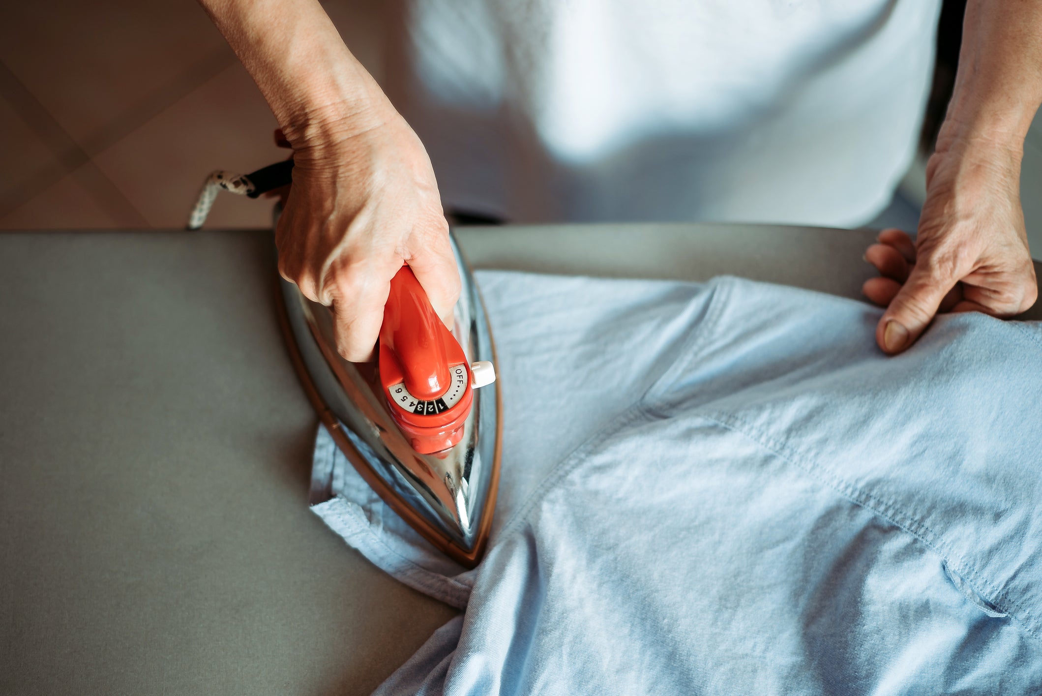 A hand holds an iron over a shirt lying on an ironing board