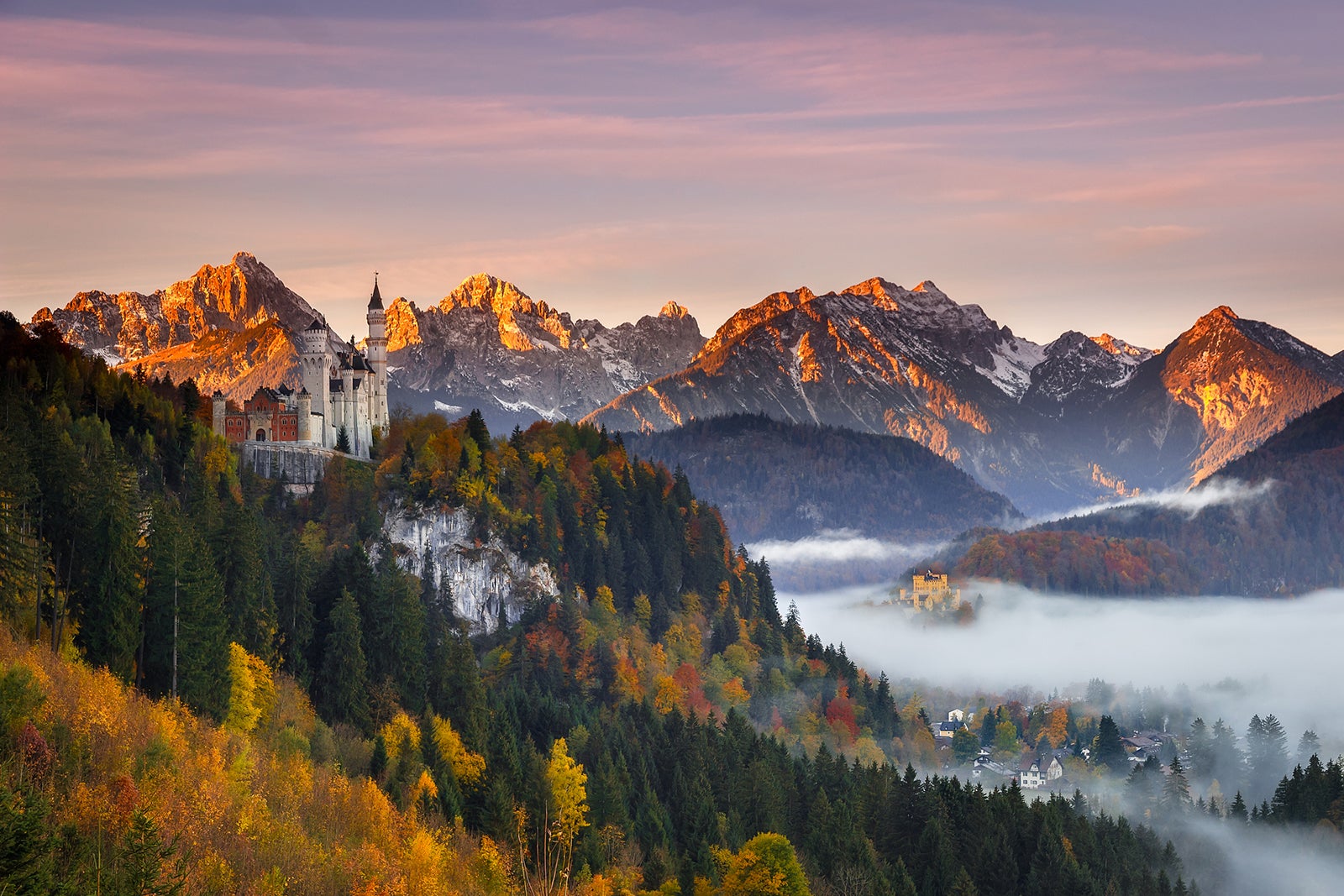 Neuschwanstein Castle surrounded by fall foliage with mountains behind