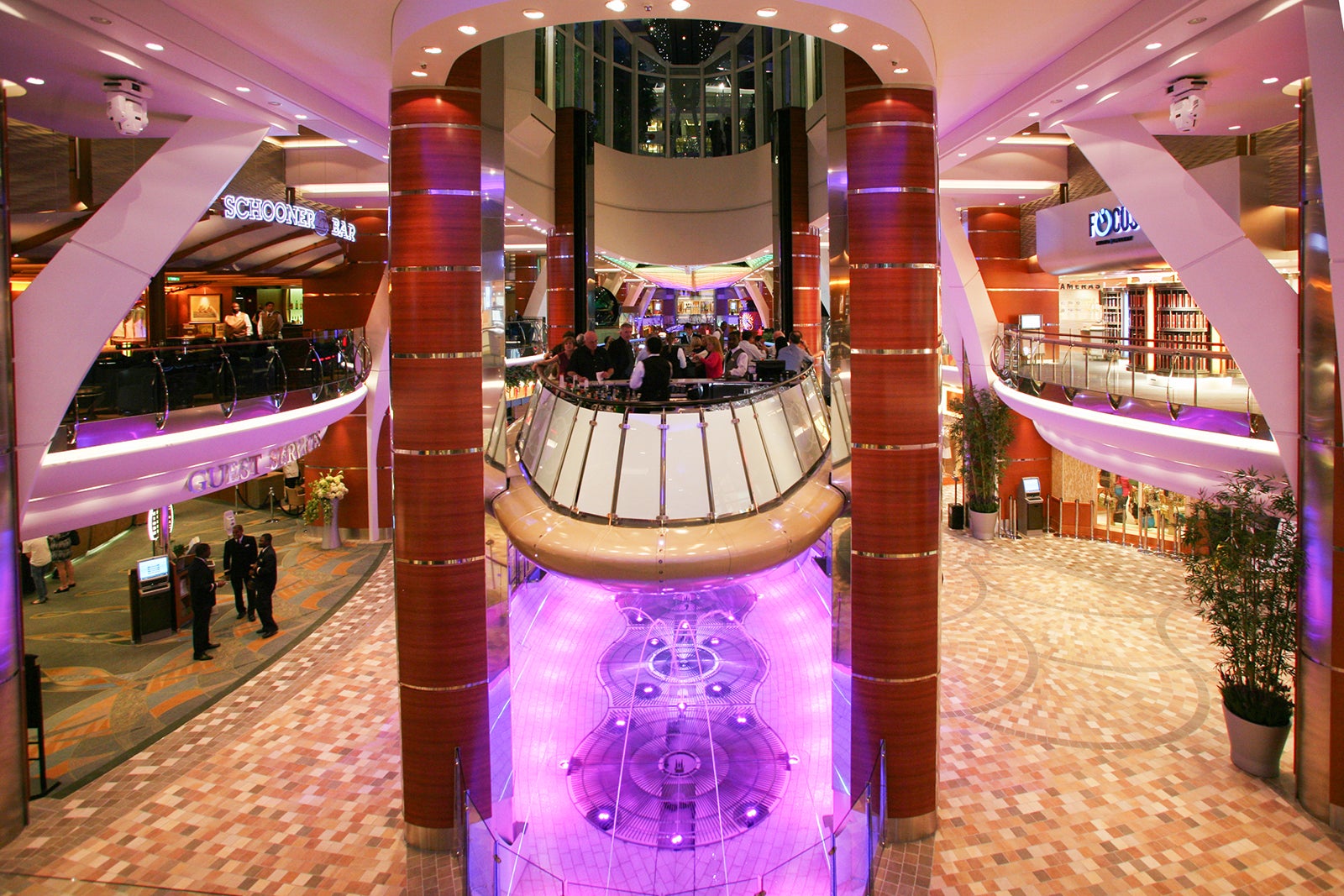 A bar with a fountain underneath it levitating on hydraulics in the middle of a shopping mall-like promenade on a cruise ship