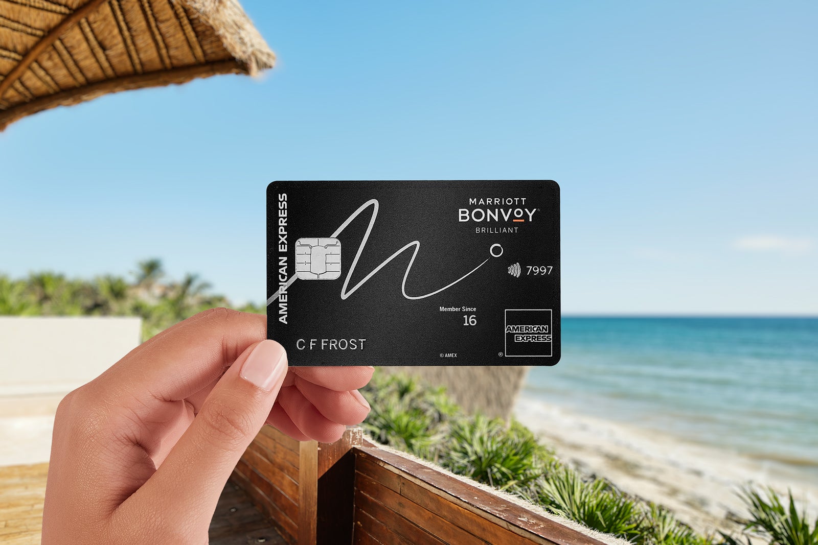 a hand holds a credit card near a beach