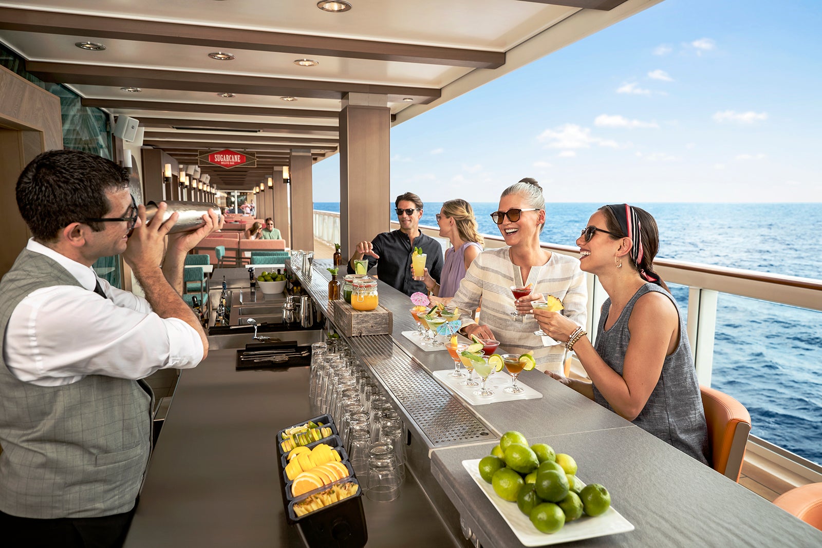 people sitting at an open-air cruise ship bar enjoying mojitos while a bartender mixes a drink