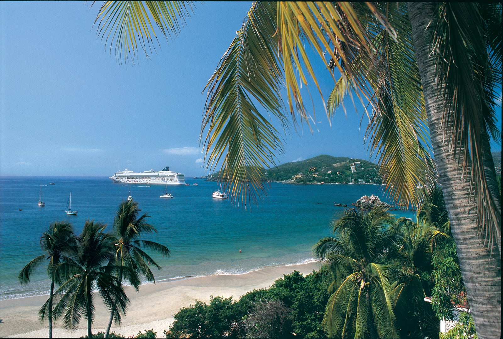 Norwegian Star cruise ship anchored off the sandy beaches and palm trees of Zihuatanejo, Mexico