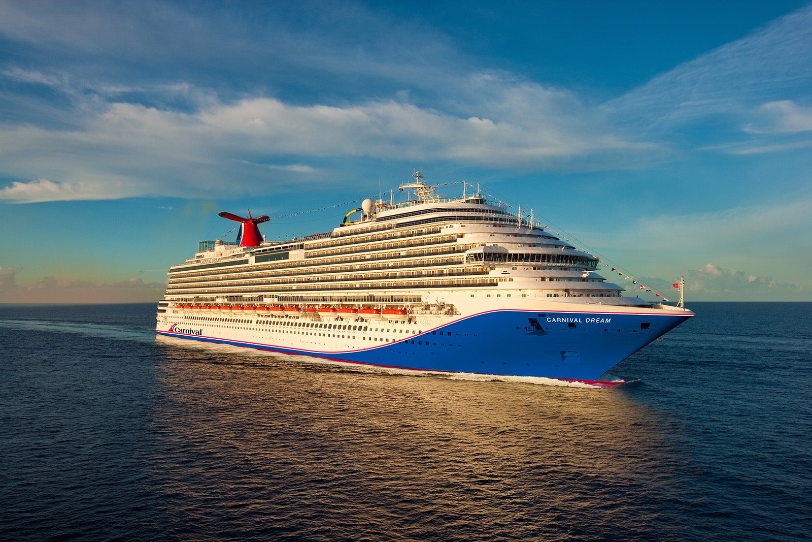 A white ship with a blue hull sailing on blue water with blue sky and clouds in the background