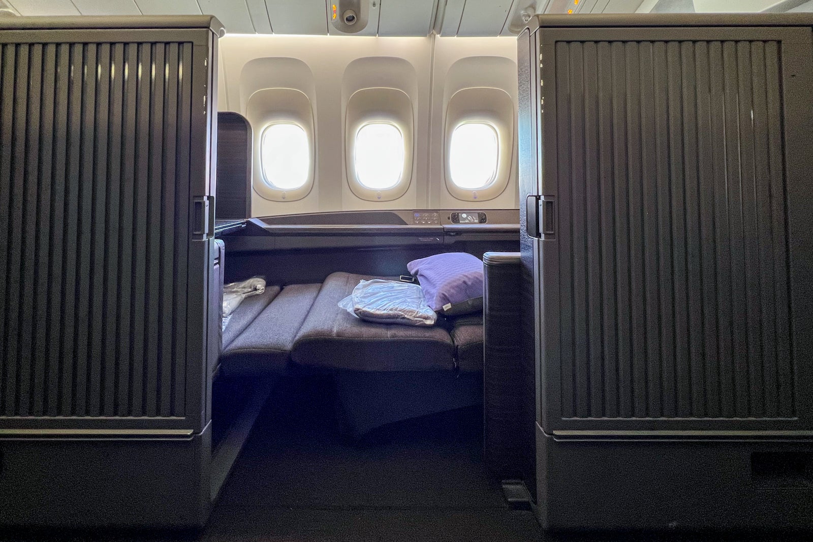 a mini-suite in an airplane's first class cabin shows the door open and seat reclined into the bed position