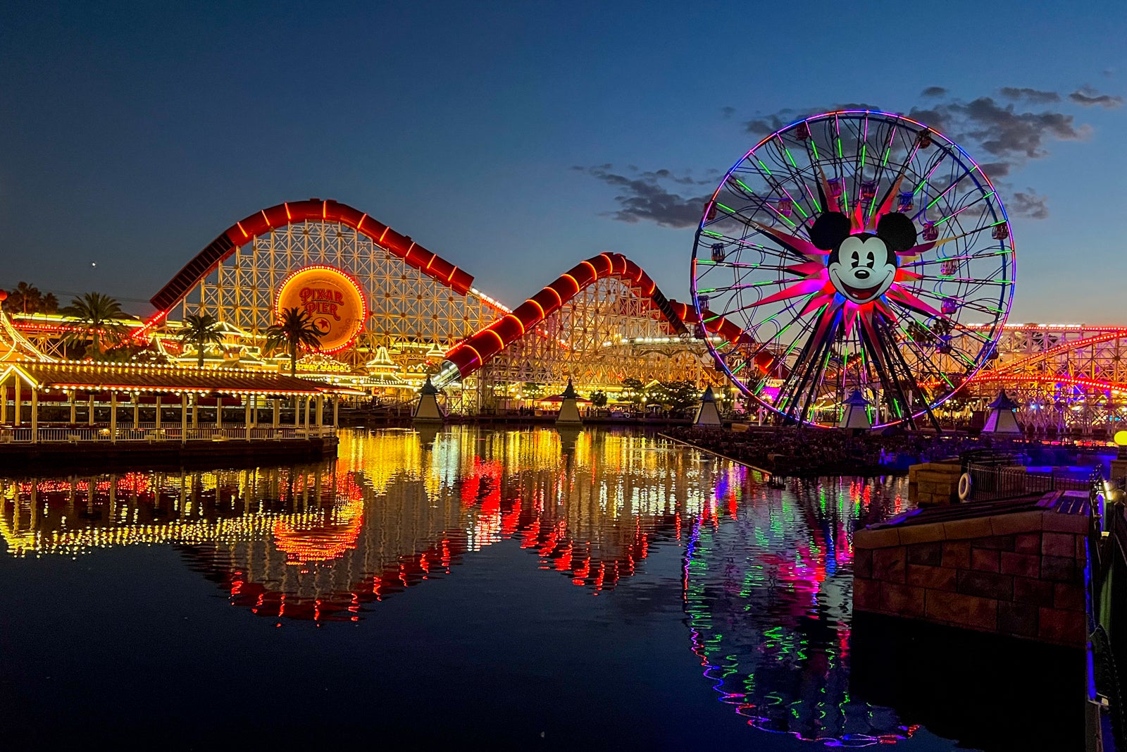 the roller coasters and Ferris wheel at California Adventure Park are lit up at night and reflected in the water at Disneyland