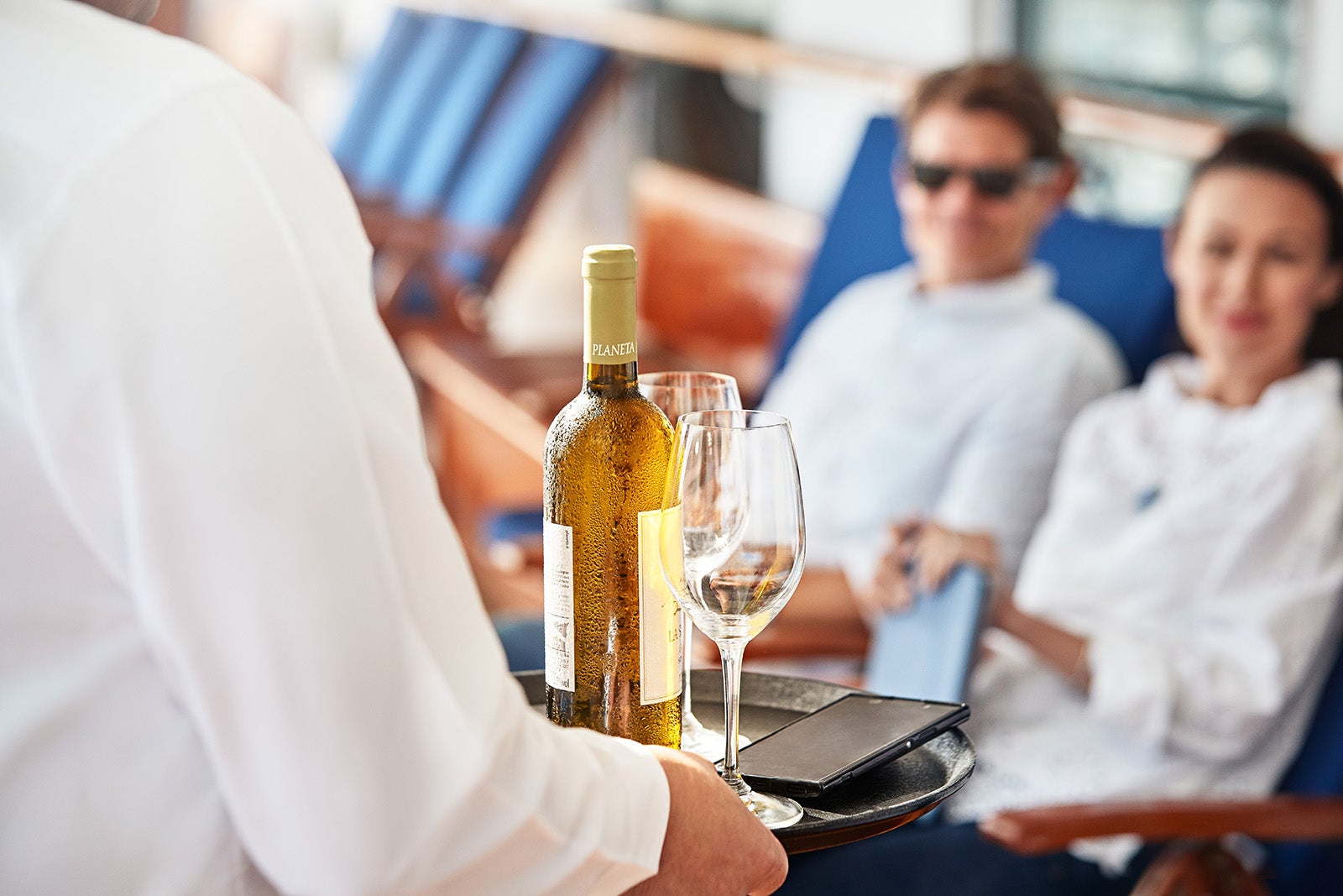 Crew member bringing bottle of white wine to couple on cruise ship deck