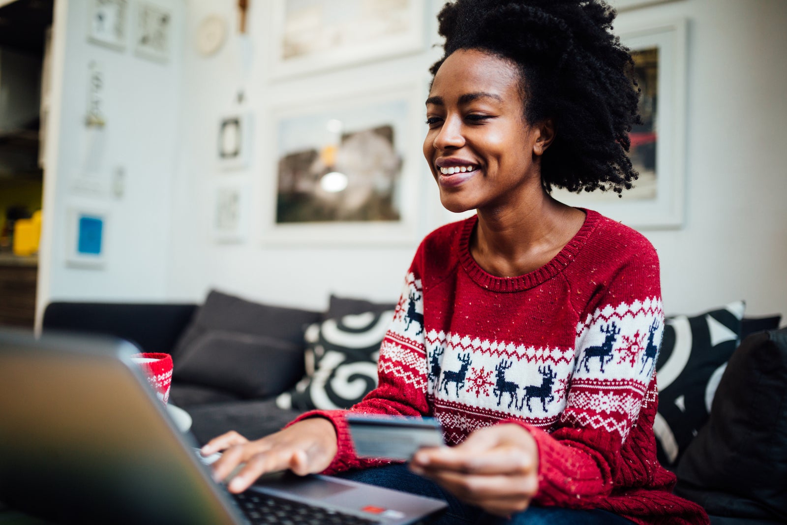 Beautiful African American woman shopping online from her cozy home office during winter holidays, holding a credit card while purchasing something online using a laptop