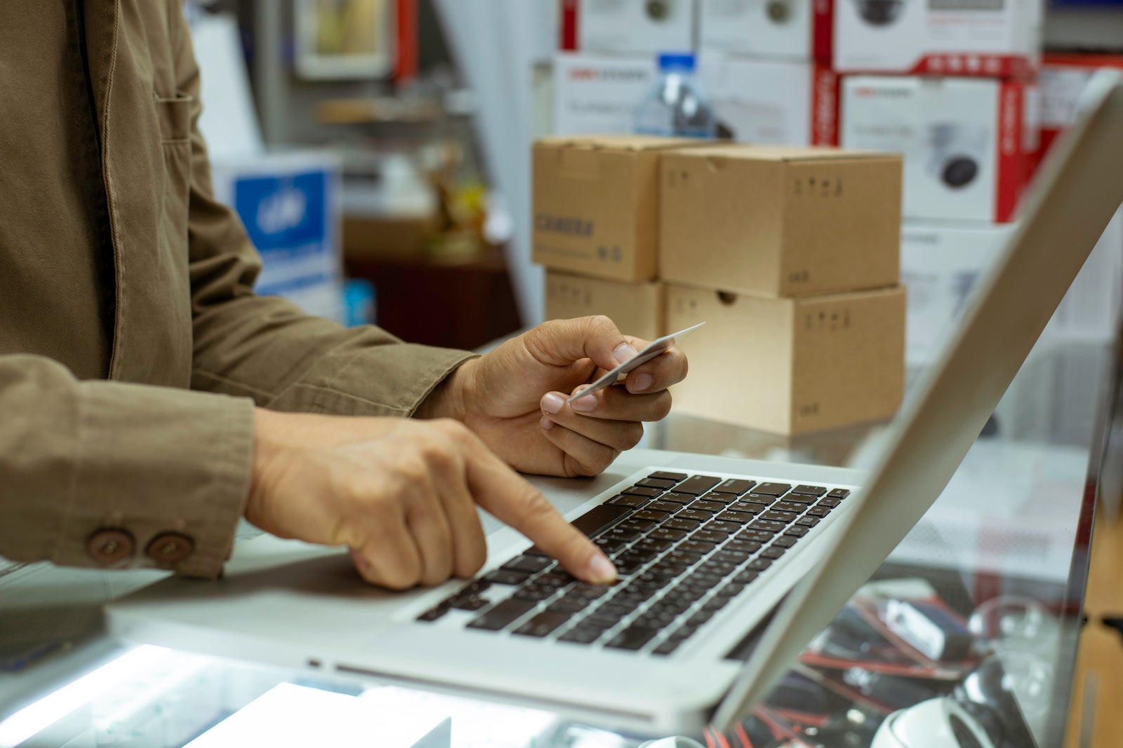 an unseen person holds a credit card while typing on a computer