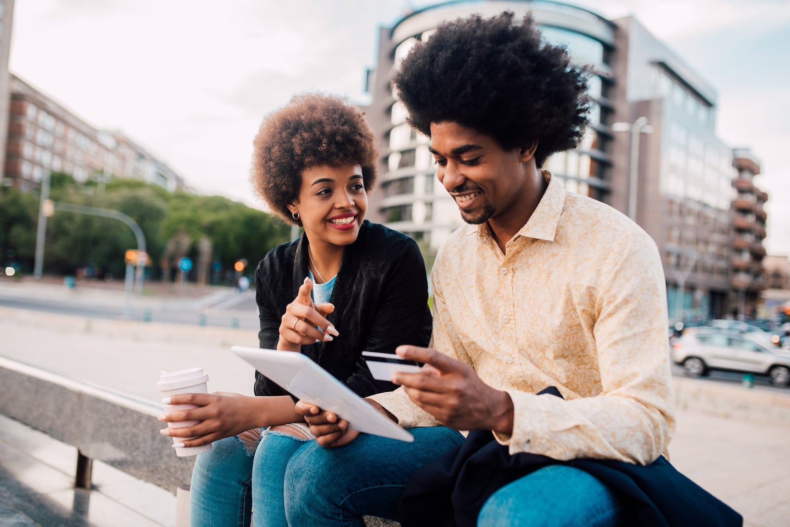 a young couple sits on steps outdoors while comparing credit cards