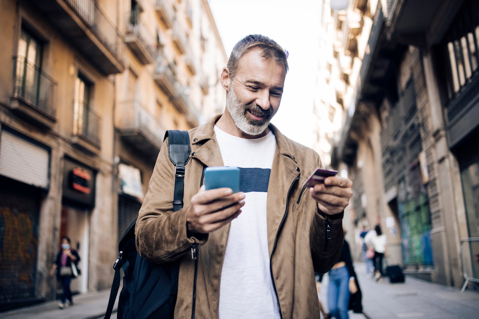 a middle-aged man holds a credit card while looking at his phone