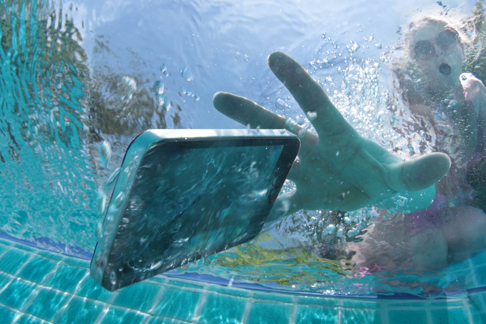 view from inside a swimming pool as a person reaches for a phone that just fell into the water