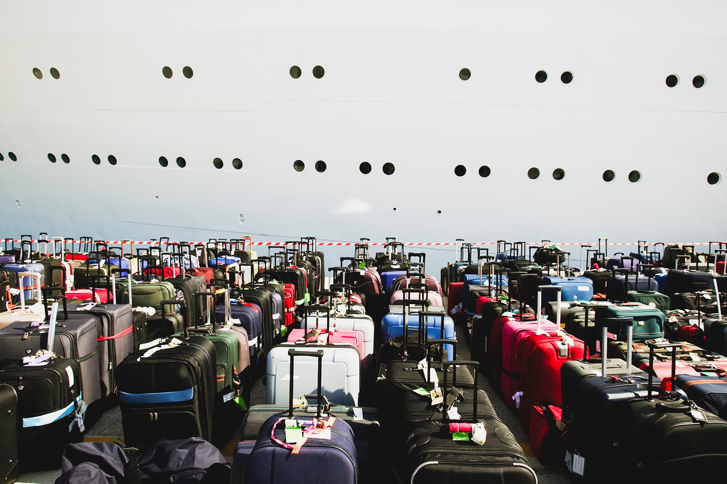 Dozens of suitcases sit in rows on the dock in front of the side of a cruise ship