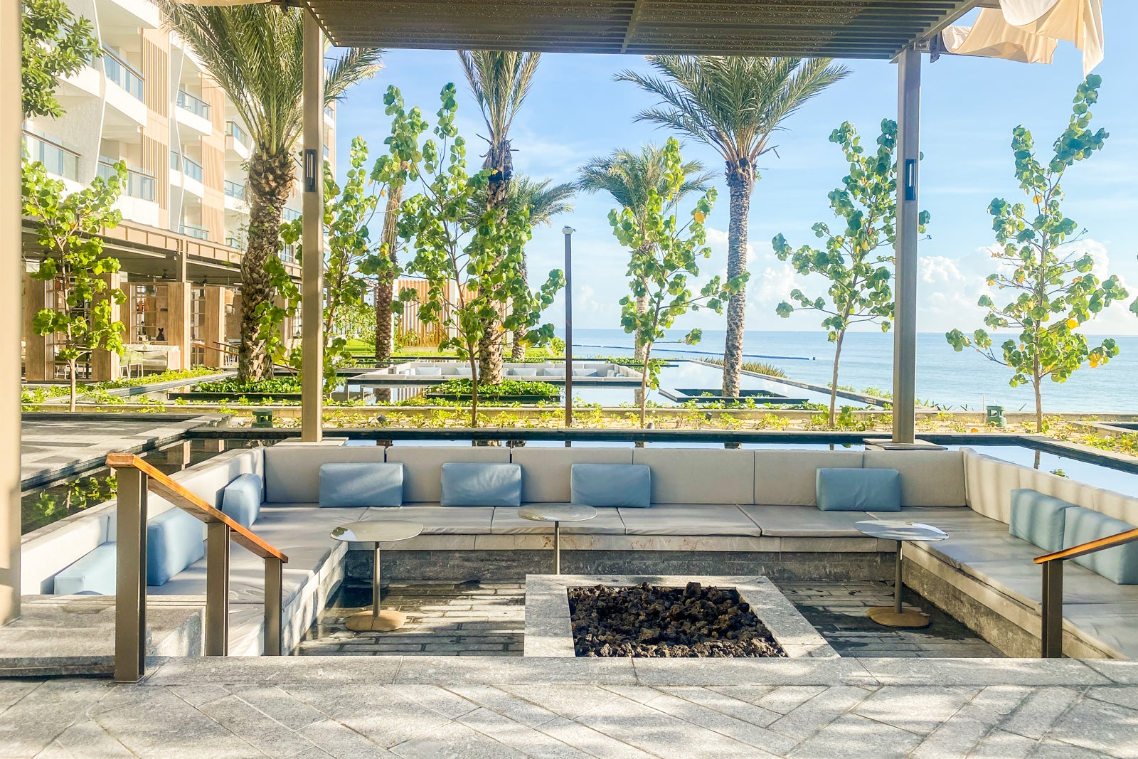 benches surrounded a fire pit with many palm trees nearby, looking out over the ocean