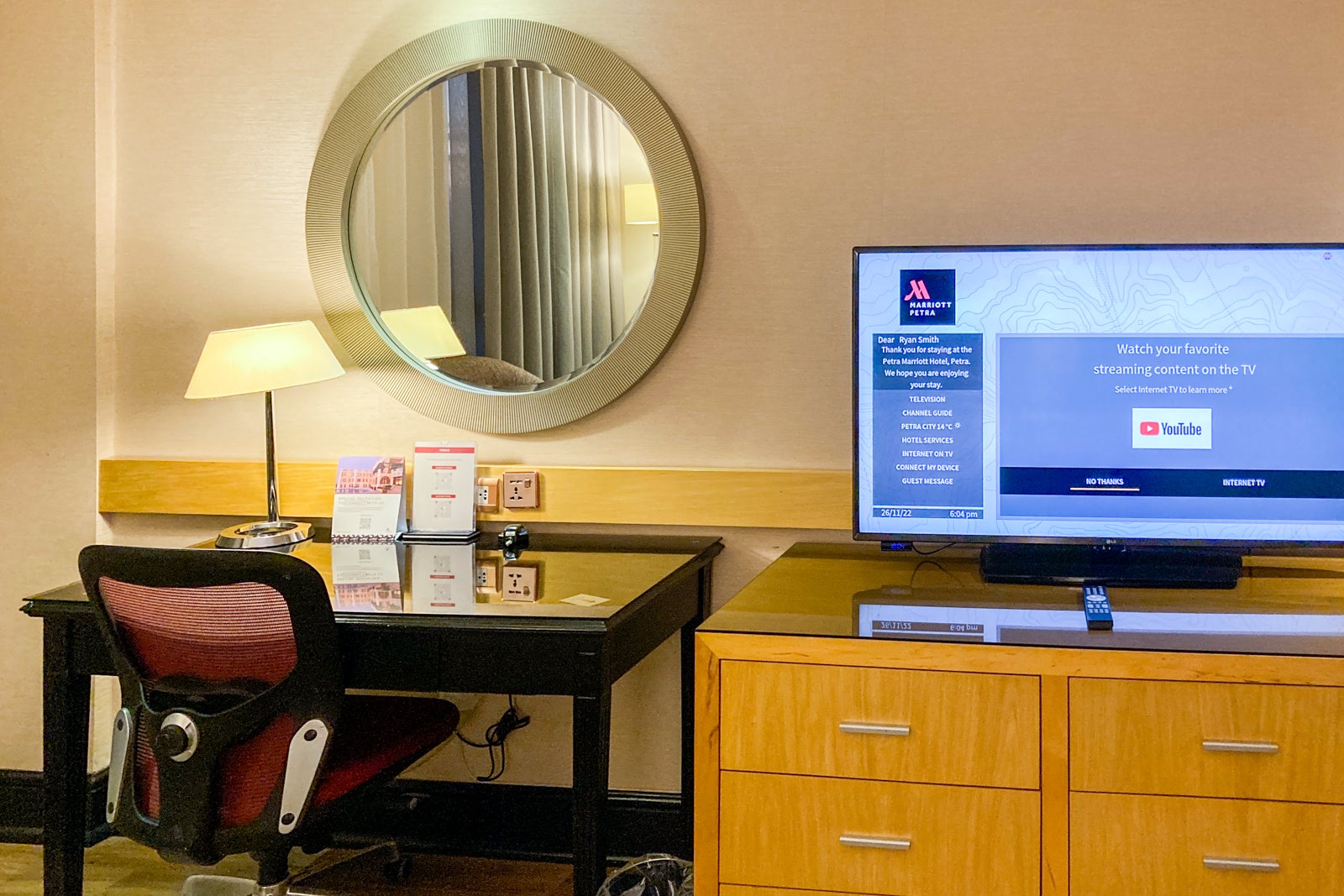 a tv sits on a dresser, which is next to a desk and chair in a hotel room