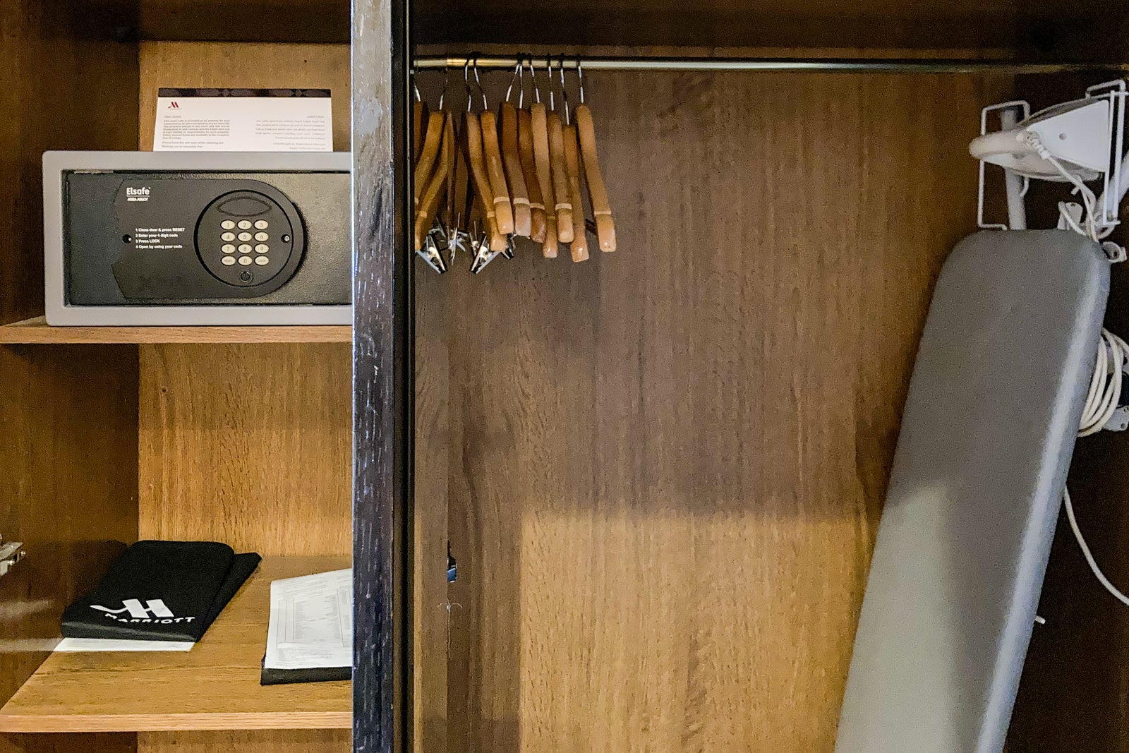 a small safe, shelving, ironing board and hangers inside a closet