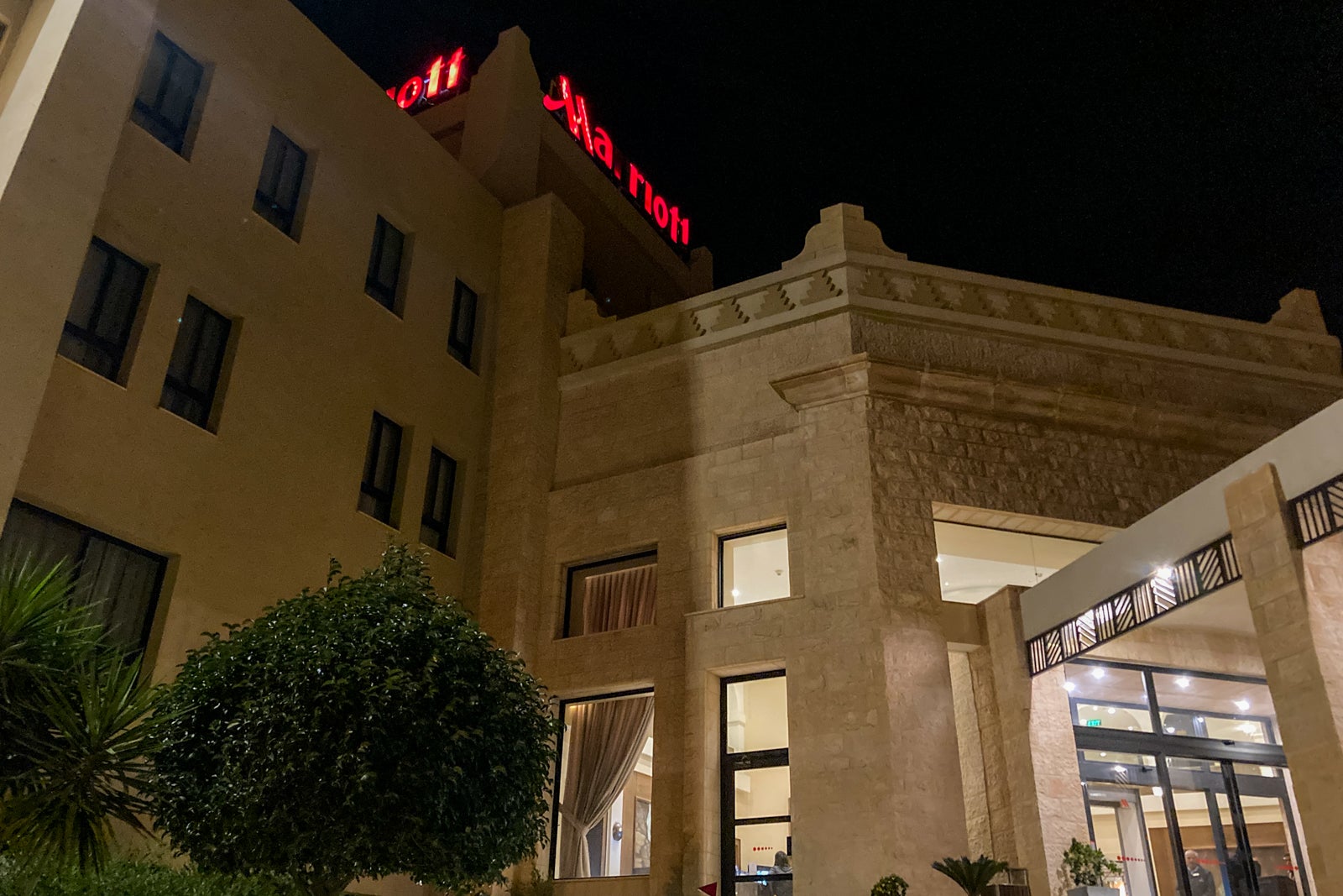 looking up at the entrance to the Petra Marriott Hotel at night, with a lit Marriott logo on top of the hotel