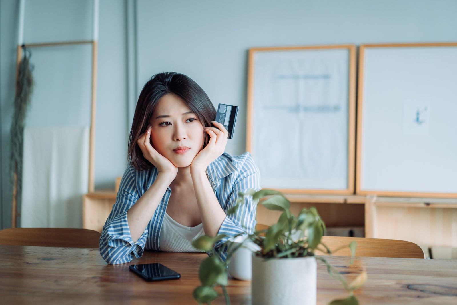 A young Asian woman looks worried as she holds a credit card