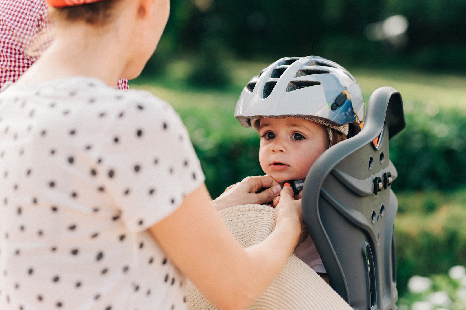 a parent puts a helmet on a child who is sitting in a child's seat attached to the parent's bicycle