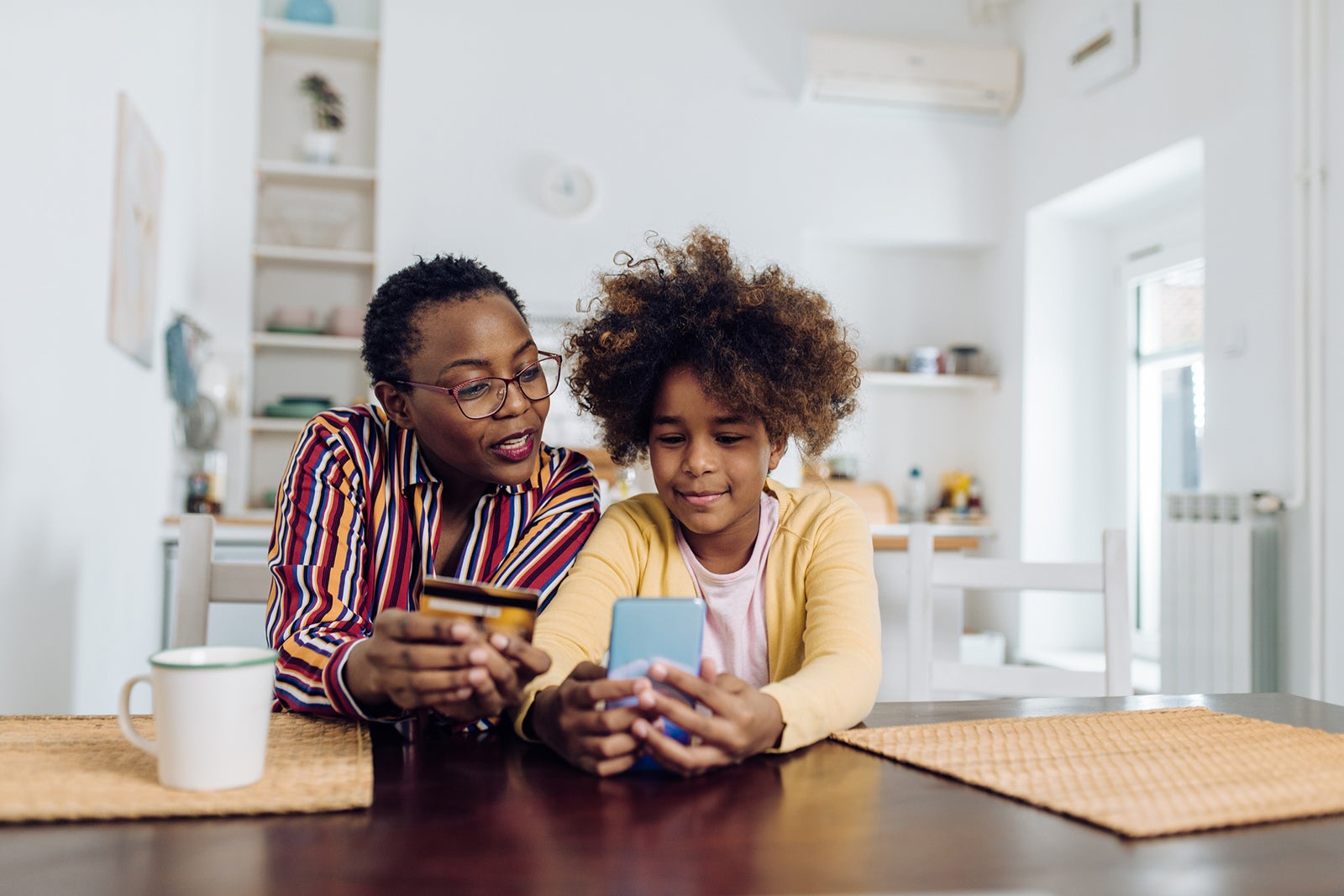 A woman and daughter with a phone and credit card sitting together at a table