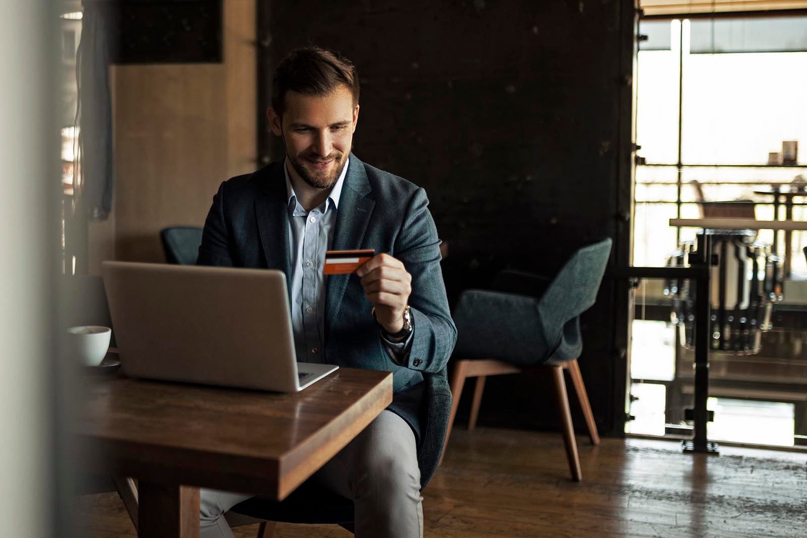 a man in a suit holds a credit card while using a laptop at his desk