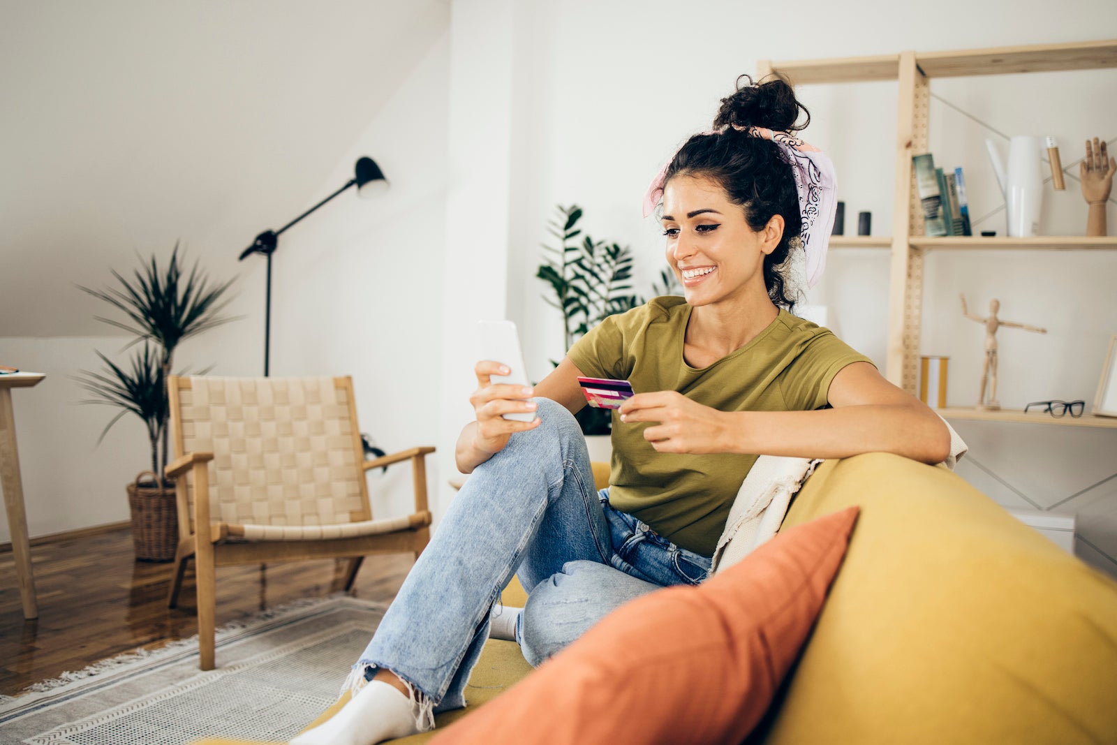 a young woman sits in her living room while using her phone to read about her credit card benefits