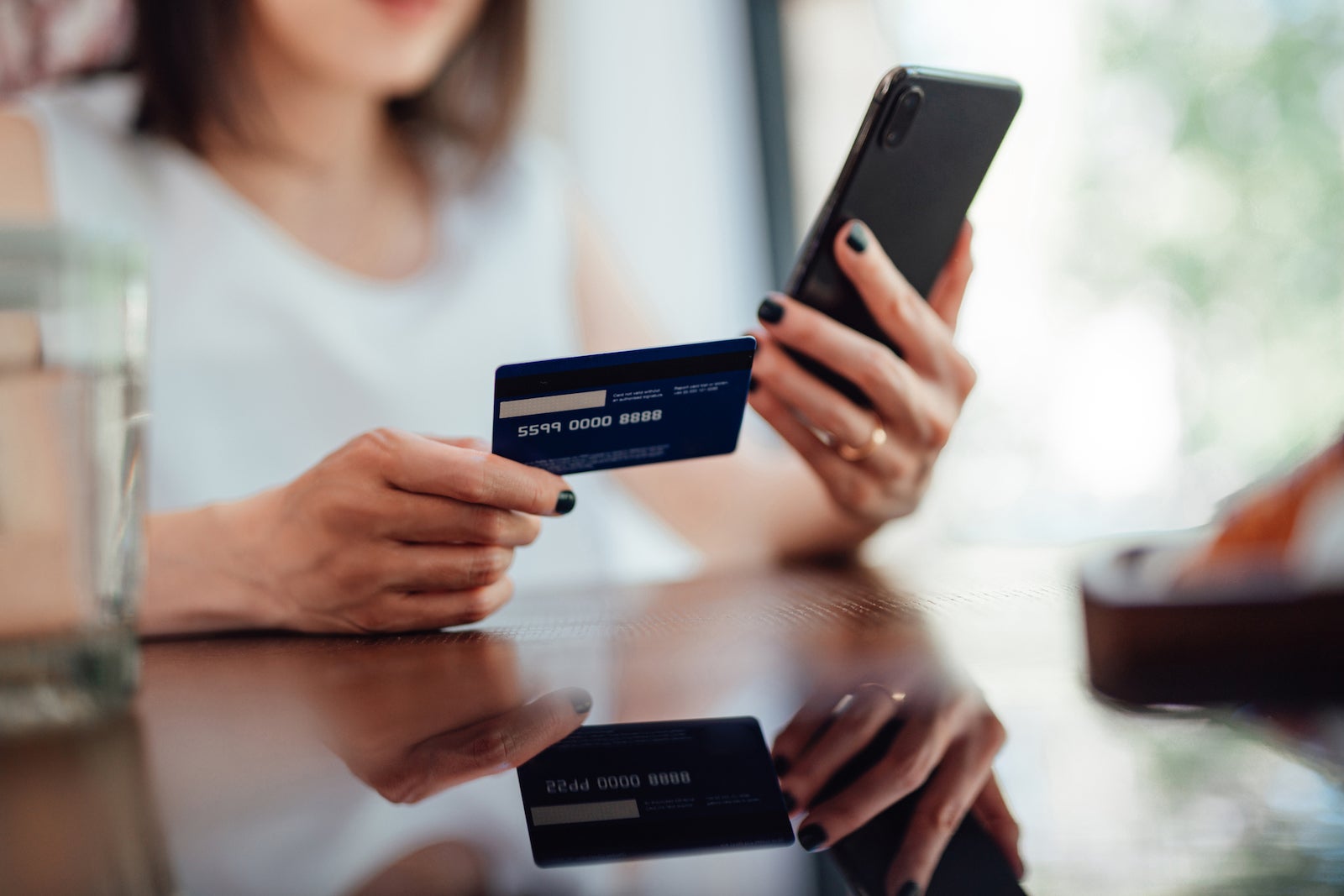 an unseen person holds a credit card and a smartphone