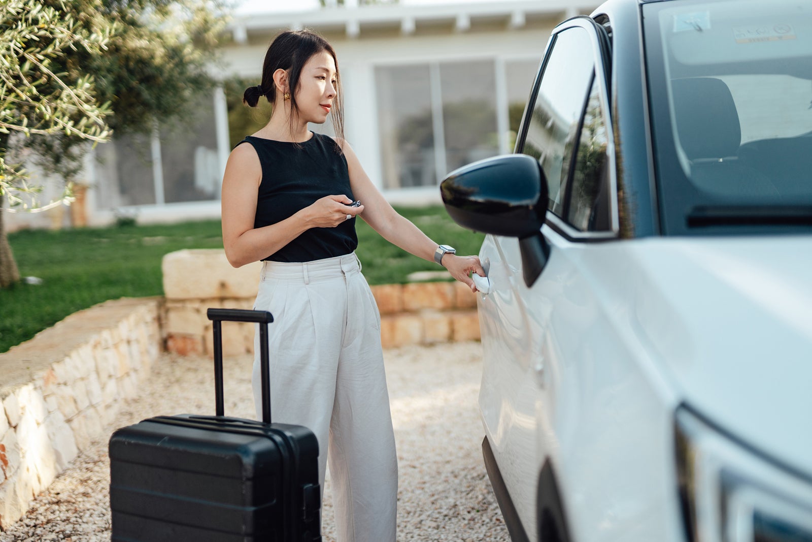 woman with large black suitcase opening door of white car