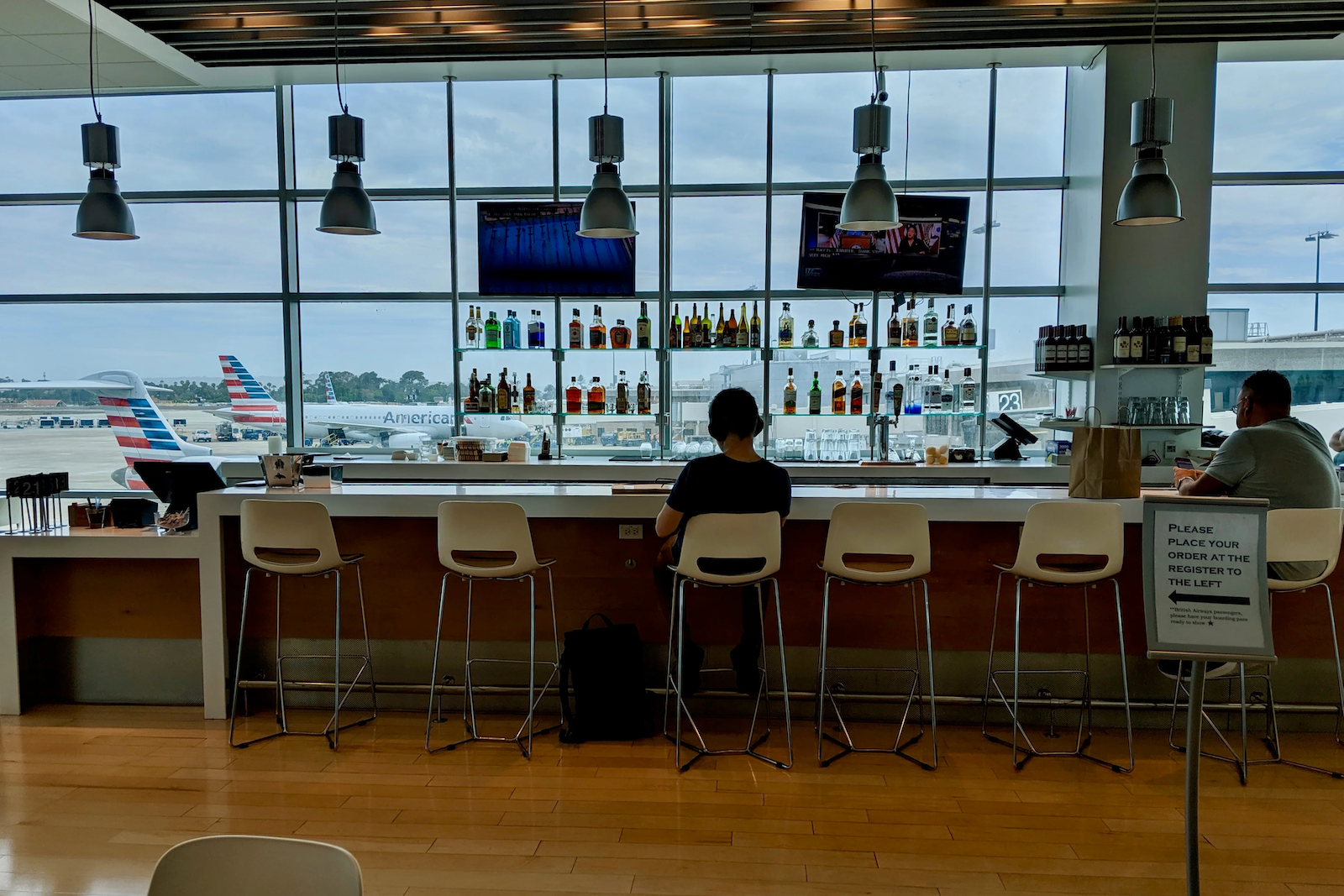 windows behind the bar in an airport lounge allow for seeing planes on the runway