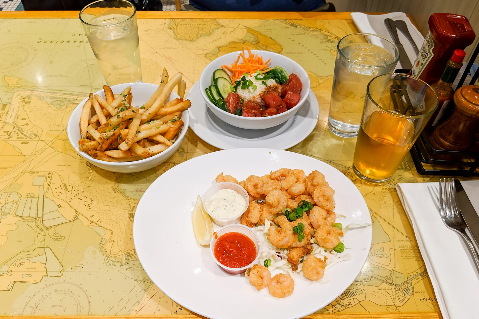 a plate of fried shrimp is flanked by a bowl of french fries and a salad bowl, sitting on a table at a restaurant