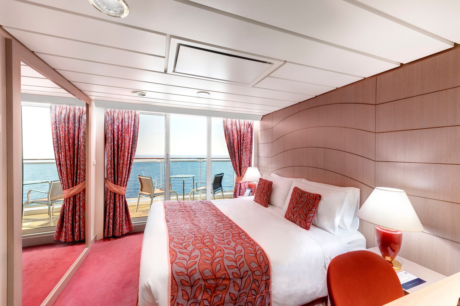 A bright cruise ship cabin with red decor and a view of the balcony 